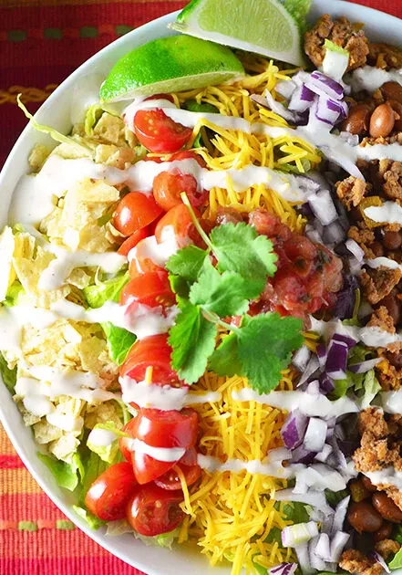A white bowl of taco salad with a lime wedge.