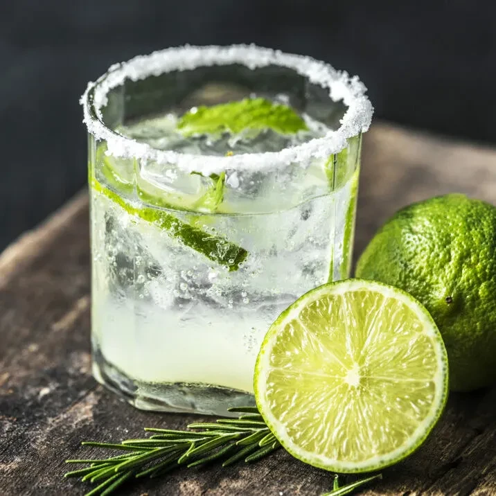 Salt-rimmed glass with lime, mint, and rosemary on a wooden surface.