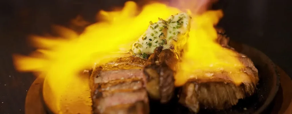 A steak with herbed butter flamed on a dark background.