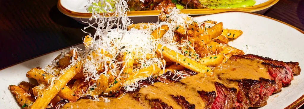 Steak with sauce and fries topped with shredded cheese and herbs.
