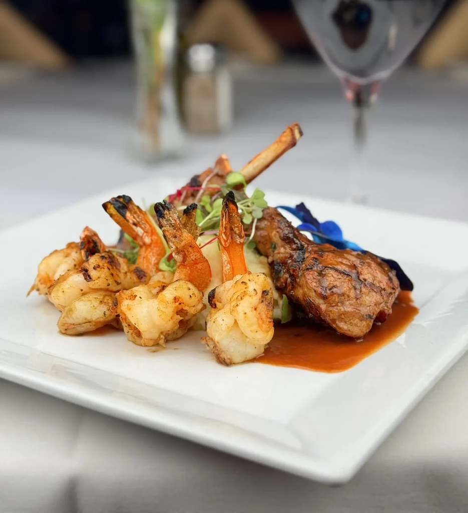 Grilled shrimp and a lamb chop on a white plate.