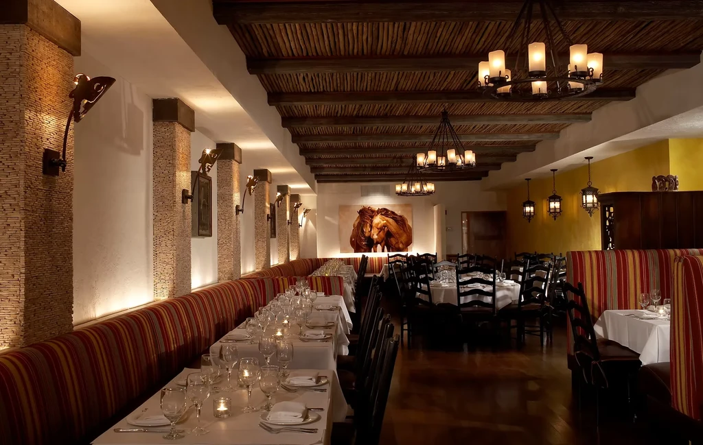 A Spanish-style restaurant with a long banquette and round tables.