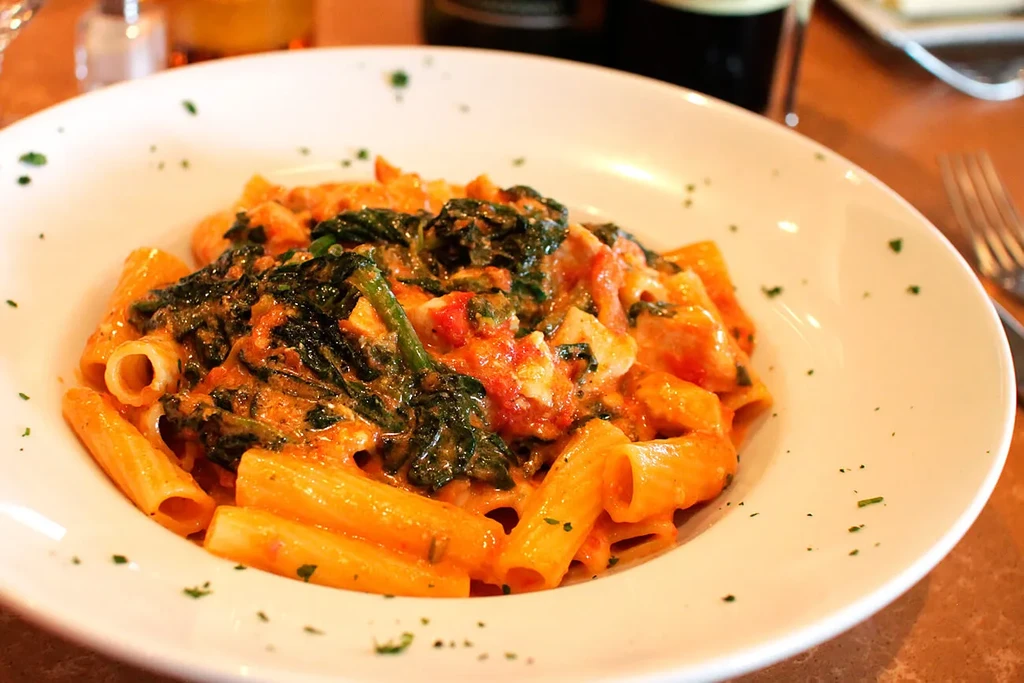 A white bowl filled with rigatoni pasta, spinach, and tomato sauce.