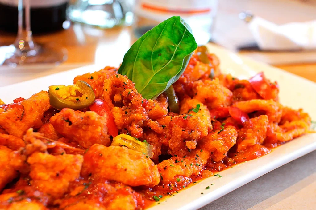 Fried calamari and peppers in tomato sauce, garnished with basil and jalapeño.