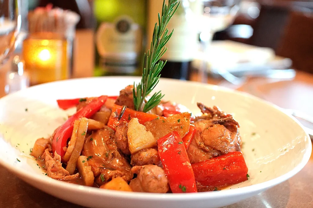 Stew with chicken, red peppers, potatoes, and a rosemary garnish.