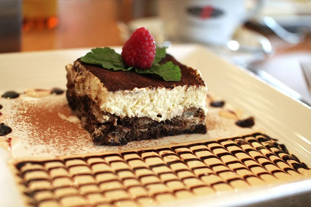 A tiramisu square with raspberry and mint on a white plate.