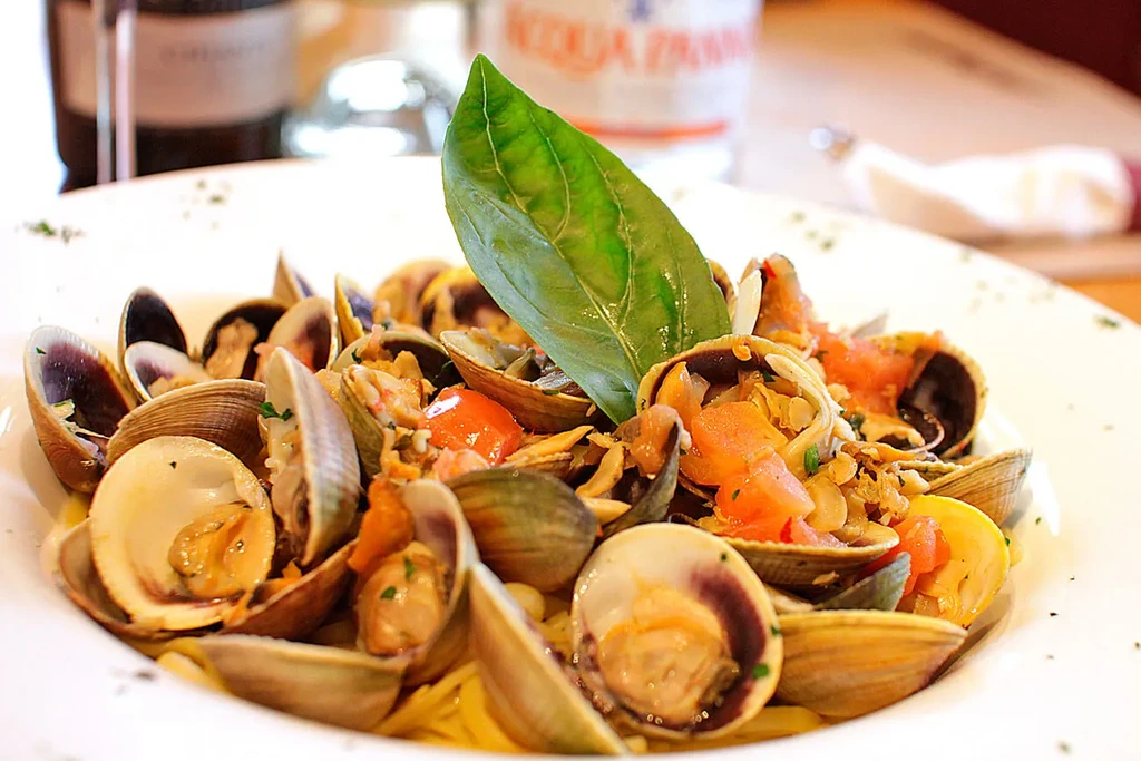 A close-up of spaghetti with clams, tomatoes, and a basil leaf.