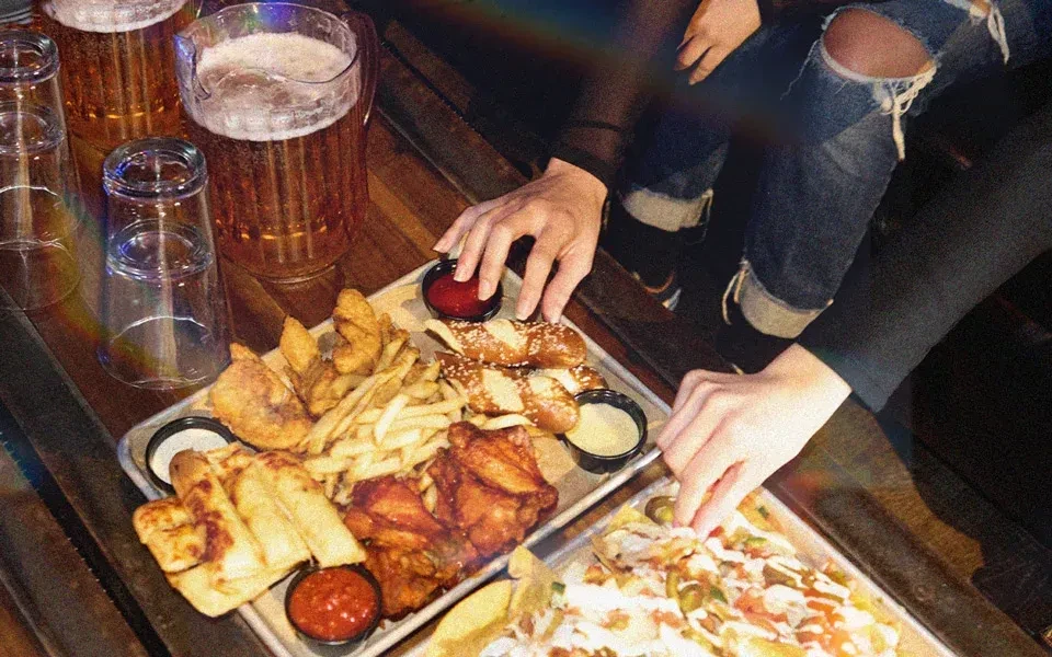 Two people sharing platters of food and pitchers of beer.