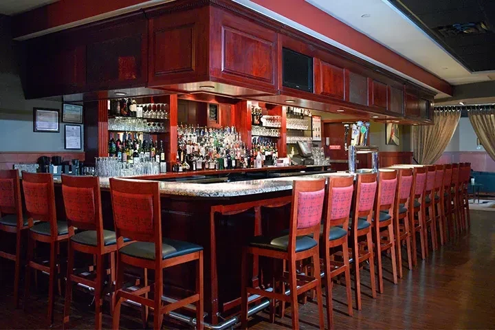 Curved dark wood bar, liquor bottles, beer taps, integrated screens, stools.