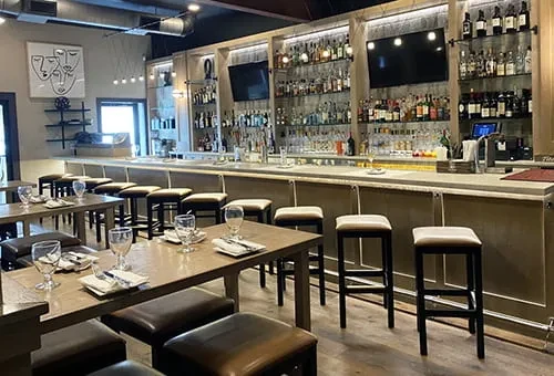 An empty restaurant with set tables, a long bar, and many liquor bottles.