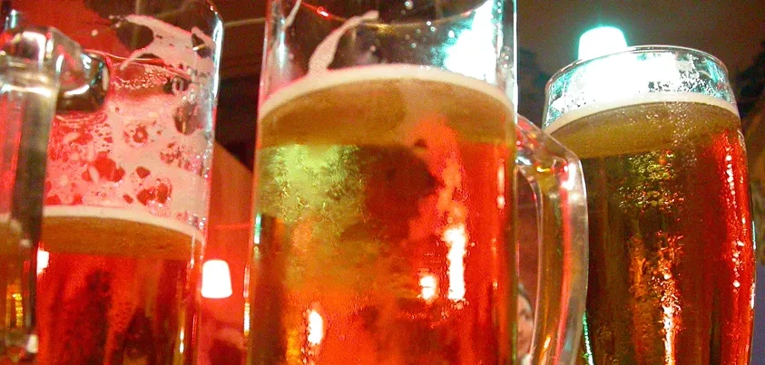 Three beer mugs with foam and condensation, illuminated by red and green light.