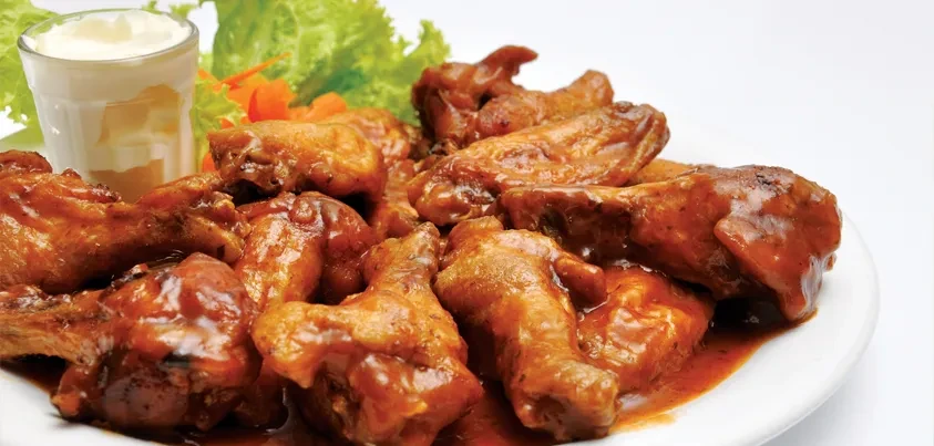 A plate of buffalo wings with sauce, lettuce, and a cup of dip.