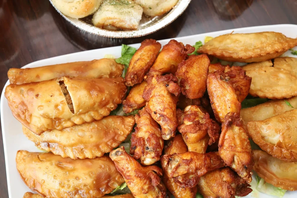 A platter of fried chicken wings and empanadas with a side of bread.
