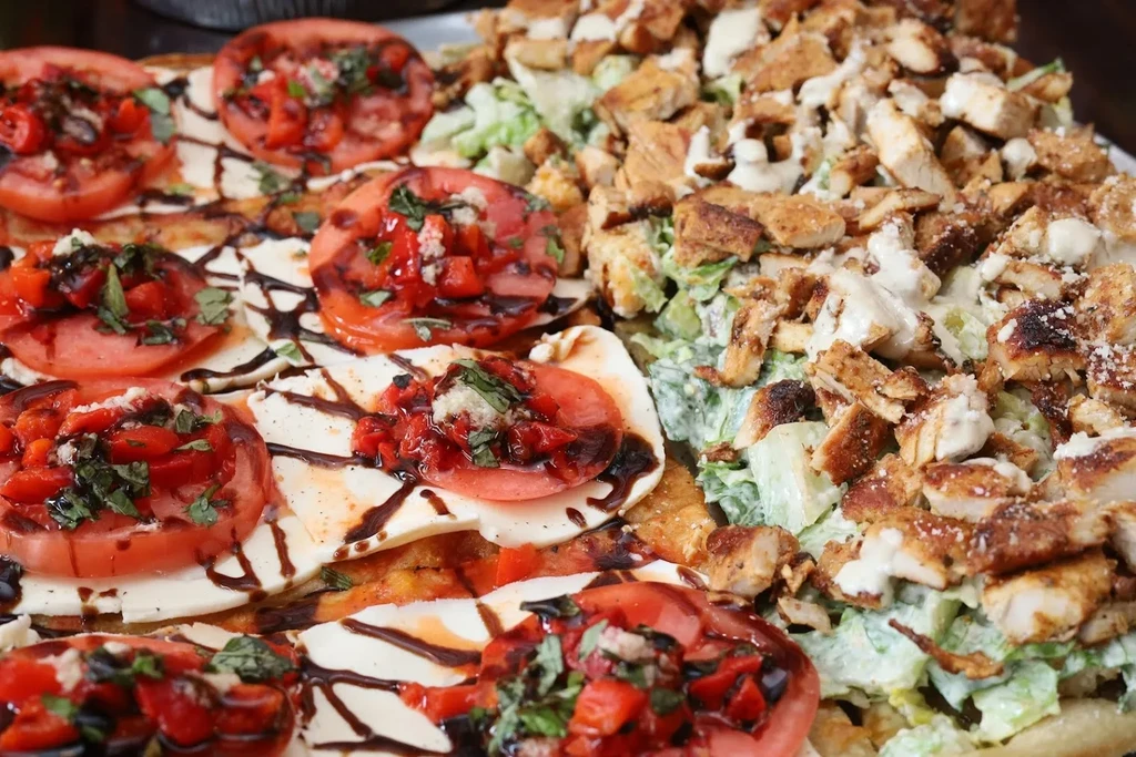 Pizza with tomatoes, mozzarella, and balsamic glaze next to Caesar salad.
