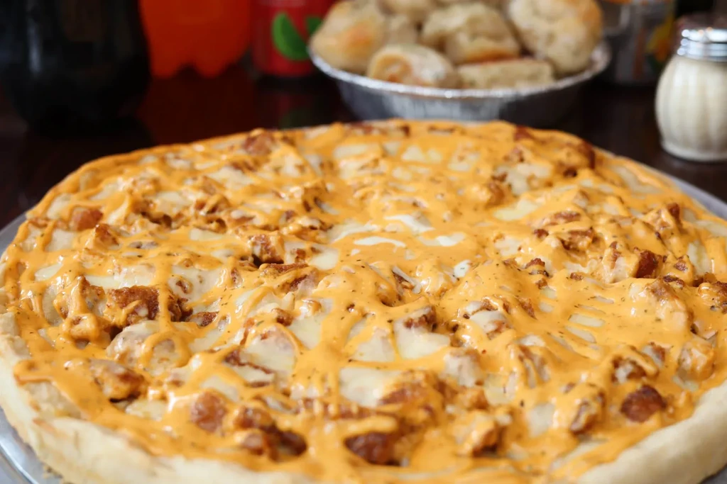 A whole pizza with white sauce and an orange drizzle.