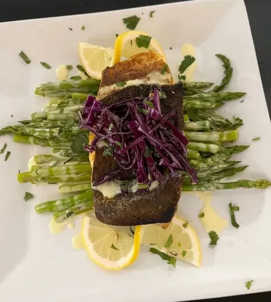 A fillet of fish with red cabbage, asparagus, and lemon on a white plate.