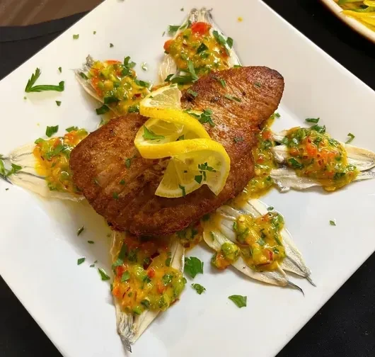 Pan-fried fish with lemon slices and sauce, surrounded by small fish.