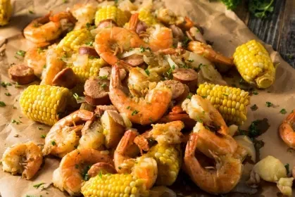 Boiled shrimp, corn, and sausage spread on brown paper.