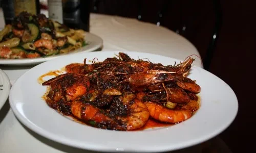 A white plate of spiced, shell-on shrimp with sauce.
