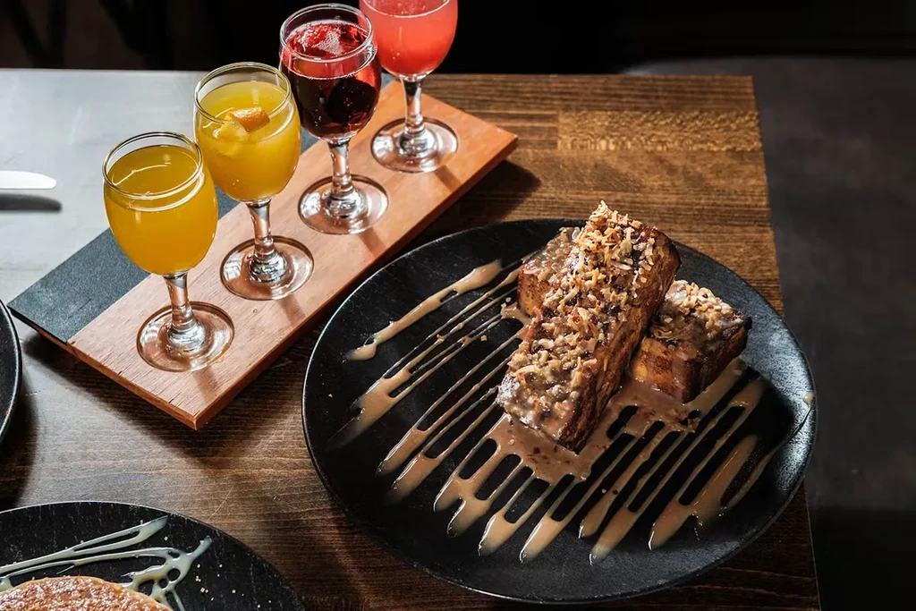 French toast with sauce and toasted coconut, and a mimosa flight on a wooden board.