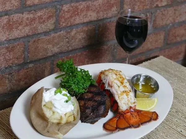 Steak and lobster dinner with baked potato and a glass of wine.