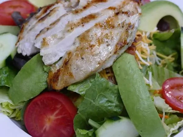 A close-up of grilled chicken salad with avocado, tomatoes, and lettuce.
