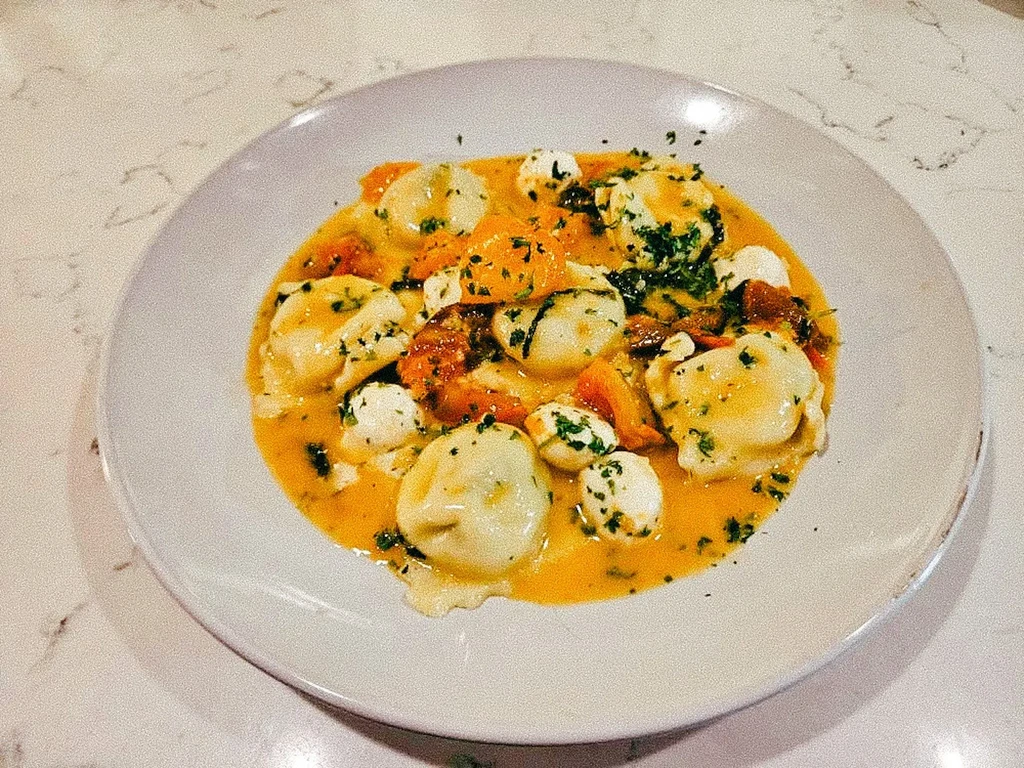 A plate of ravioli in an orange sauce with cheese and herbs.