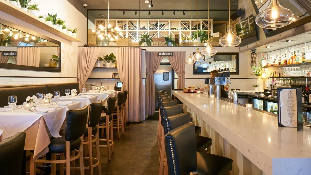 A spacious restaurant interior with a long bar and dining tables.