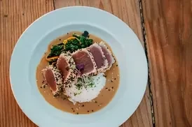 Seared tuna, rice, and greens with sauce on a white plate.
