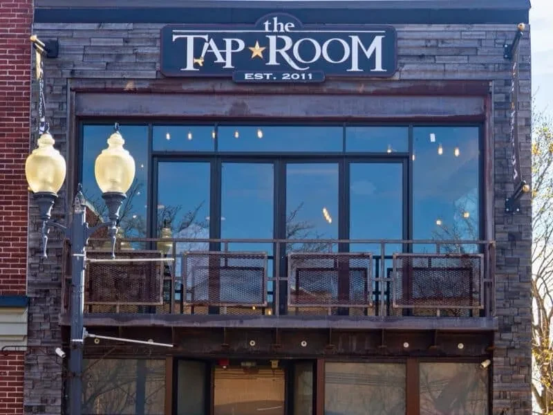 Rustic stone 'The Tap Room' building facade with balcony and large window.