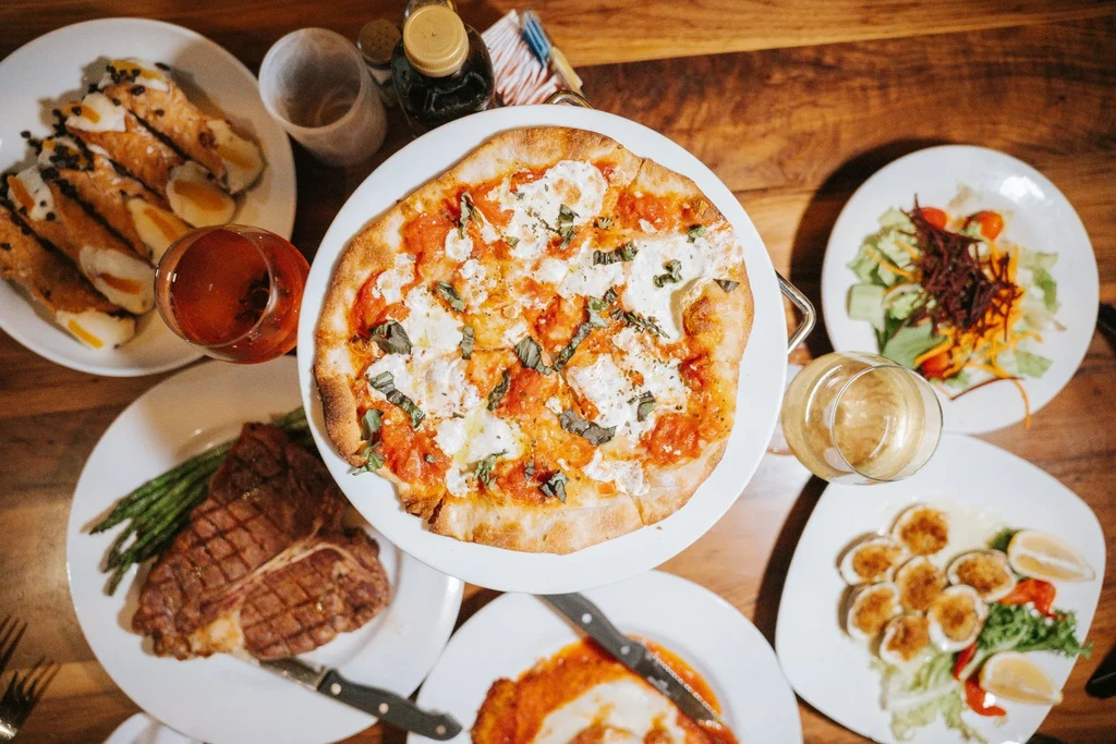 Overhead view of a dinner spread with pizza, steak, and cannolis.