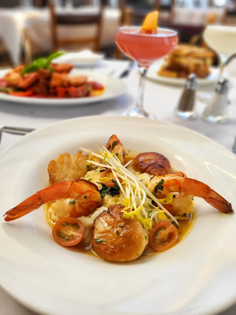 A white plate of shrimp, scallops, risotto, and vegetables on a table.