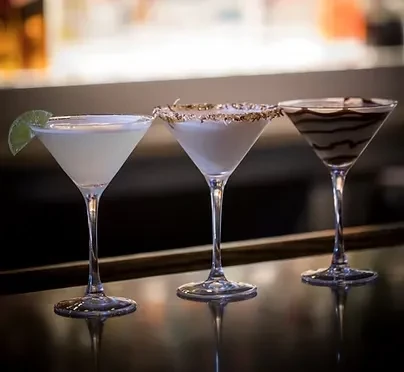 Three martini glasses with different cocktails on a bar counter.