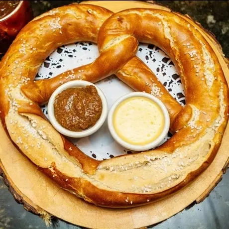 A large salted pretzel with two dipping sauces on a wooden board.