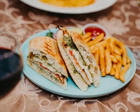 Chicken panini with pesto, mozzarella, and fries on a blue plate.