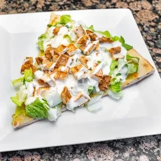 A slice of flatbread topped with grilled chicken, lettuce, and white sauce.