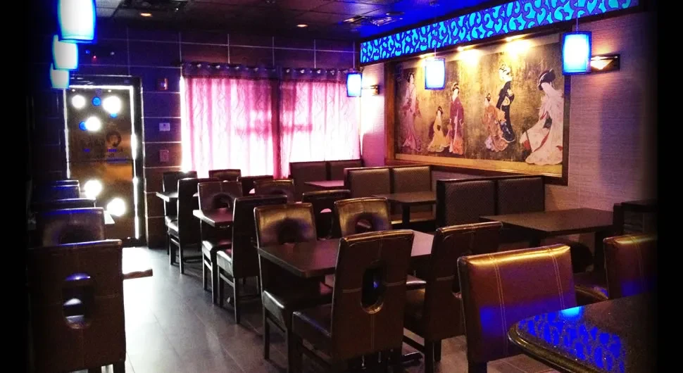 An empty restaurant with dark tables, chairs, and booths, and dim blue lighting.