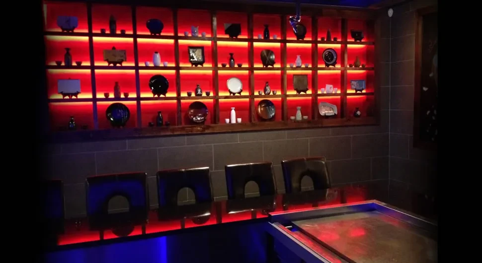 A room with a red-lit wall display of ceramics and a table.