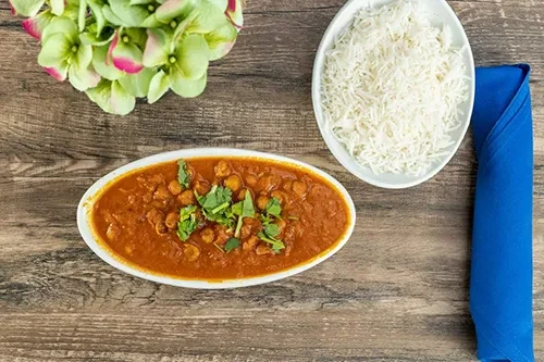 Chana masala, white rice, blue napkin, and flowers on a wooden table.