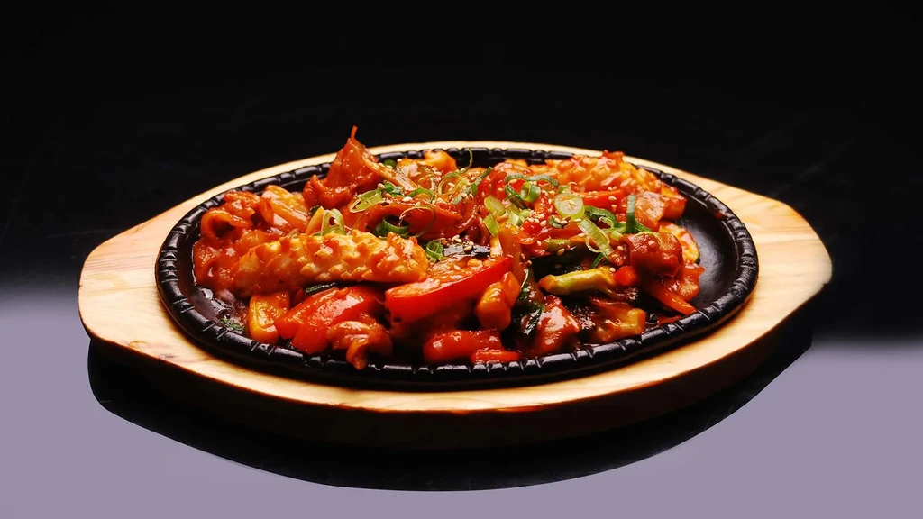 Spicy squid and vegetables served on a sizzling black plate.