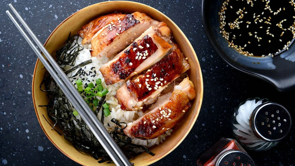 Overhead view of teriyaki chicken over rice with chopsticks and soy sauce.