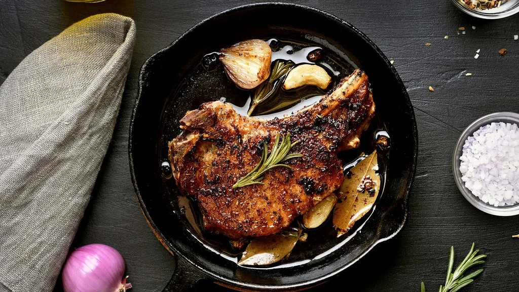 Pork chop with rosemary, garlic, and bay leaf in a cast iron skillet.