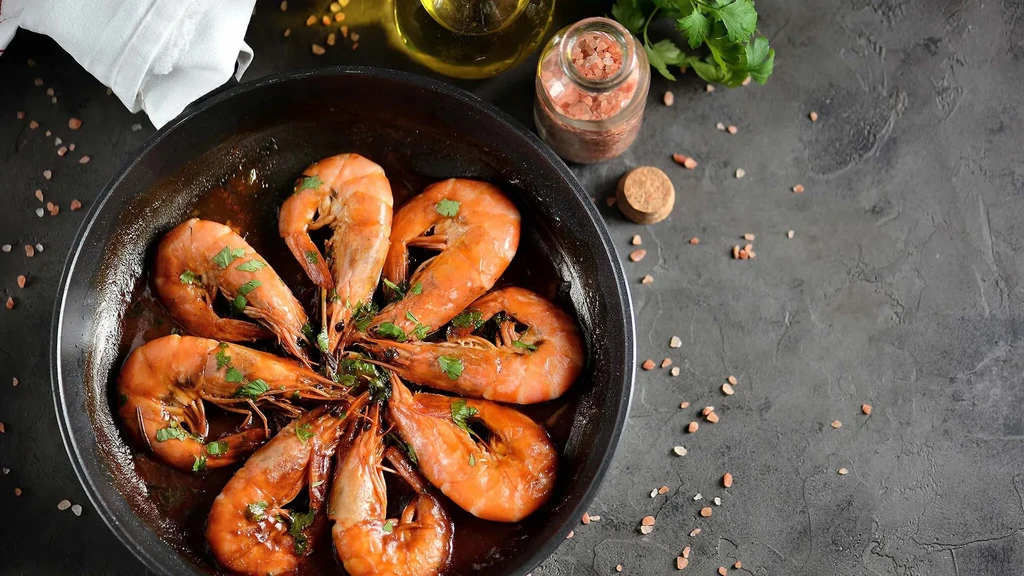 Cooked shrimp in a pan with herbs, salt, and olive oil.
