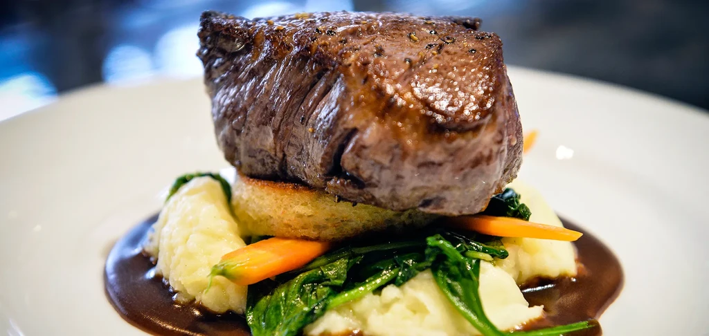 A gourmet filet mignon with mashed potatoes, spinach, carrots, and gravy.