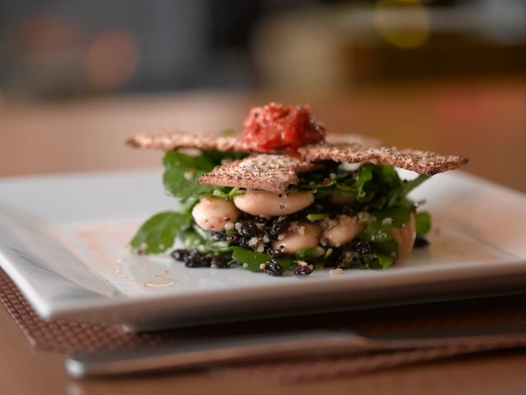 A gourmet salad with crackers, greens, beans, berries, and tomato relish.