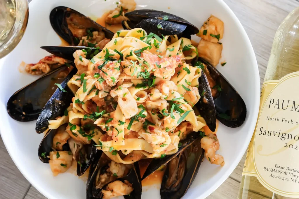 Pasta with mussels, scallops, and white wine on a white plate.