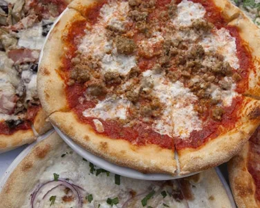 Sausage pizza with red sauce and cheese surrounded by other pizzas.