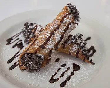 Two cannoli on a white plate, drizzled with chocolate sauce.