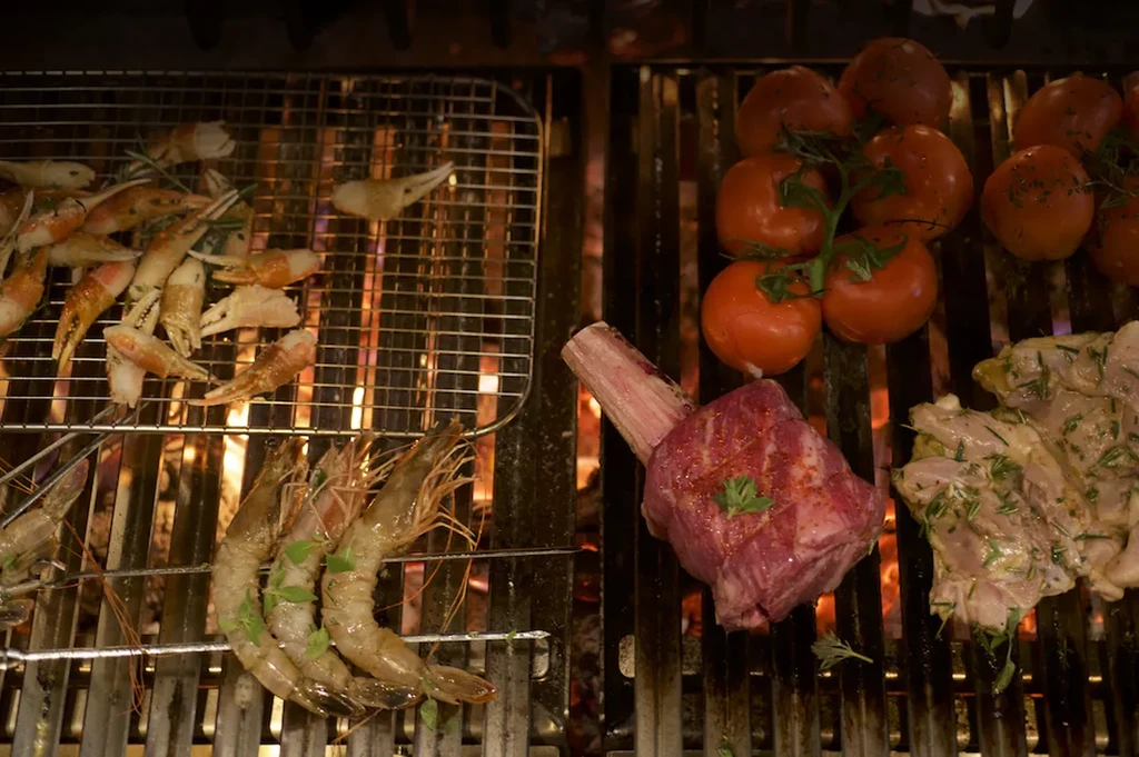 Assorted meat, seafood, and tomatoes grilling over an open flame.