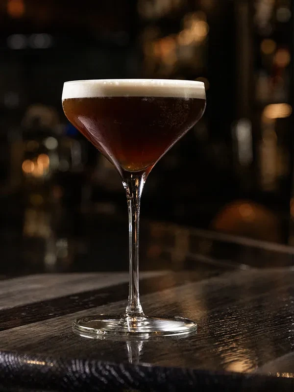 A dark cocktail with a foamy white top in a coupe glass.